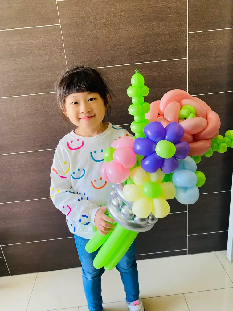 小女孩開心手捧由氣球製作的繽紛花束,包含玫瑰、雛菊與綠葉設計,氣球大叔 Sony 作品