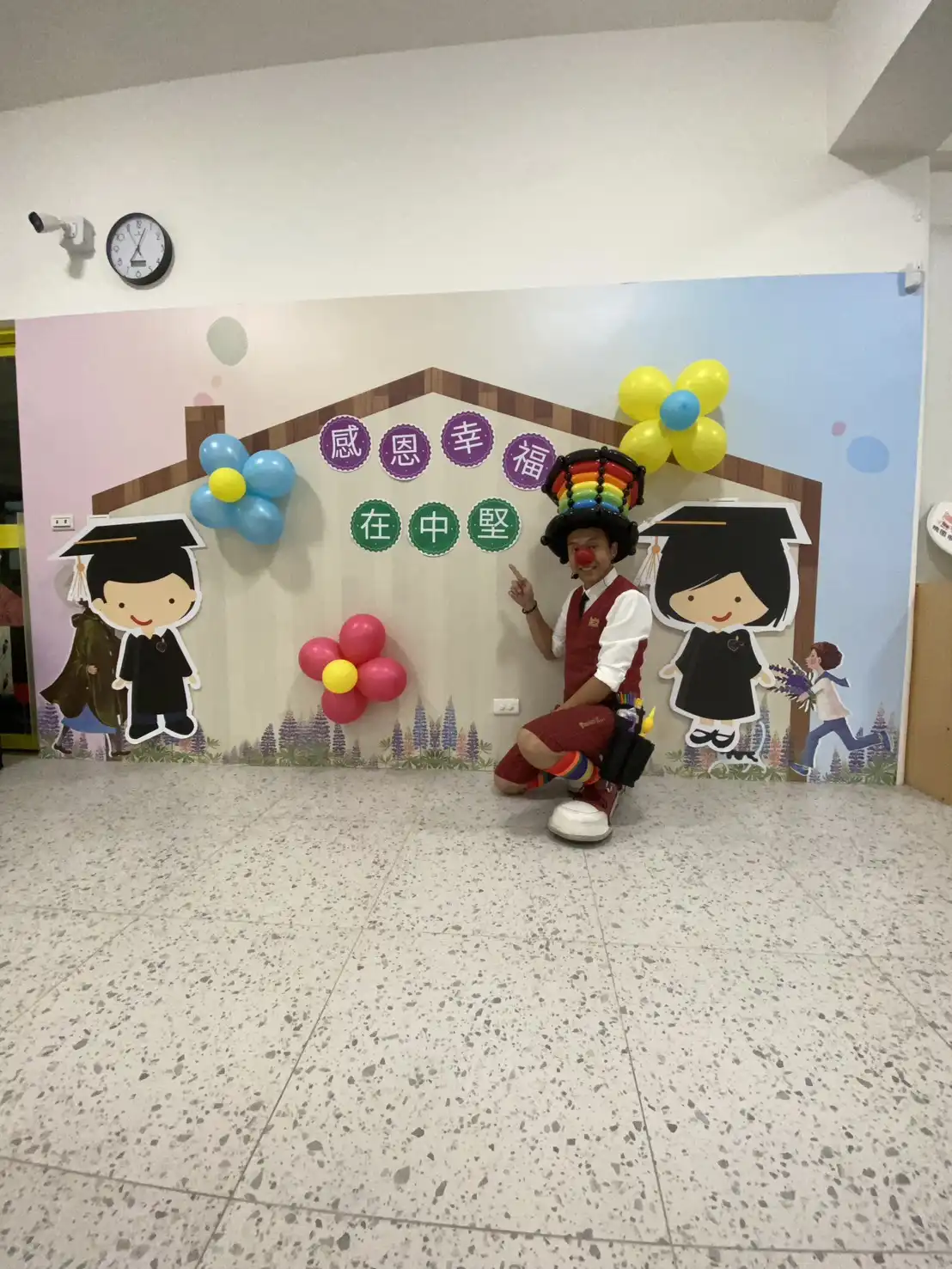 氣球大叔Sony在桃園中堅非營利幼兒園畢業典禮舞台前,與「感恩幸福在中堅」背板及畢業生立牌合影