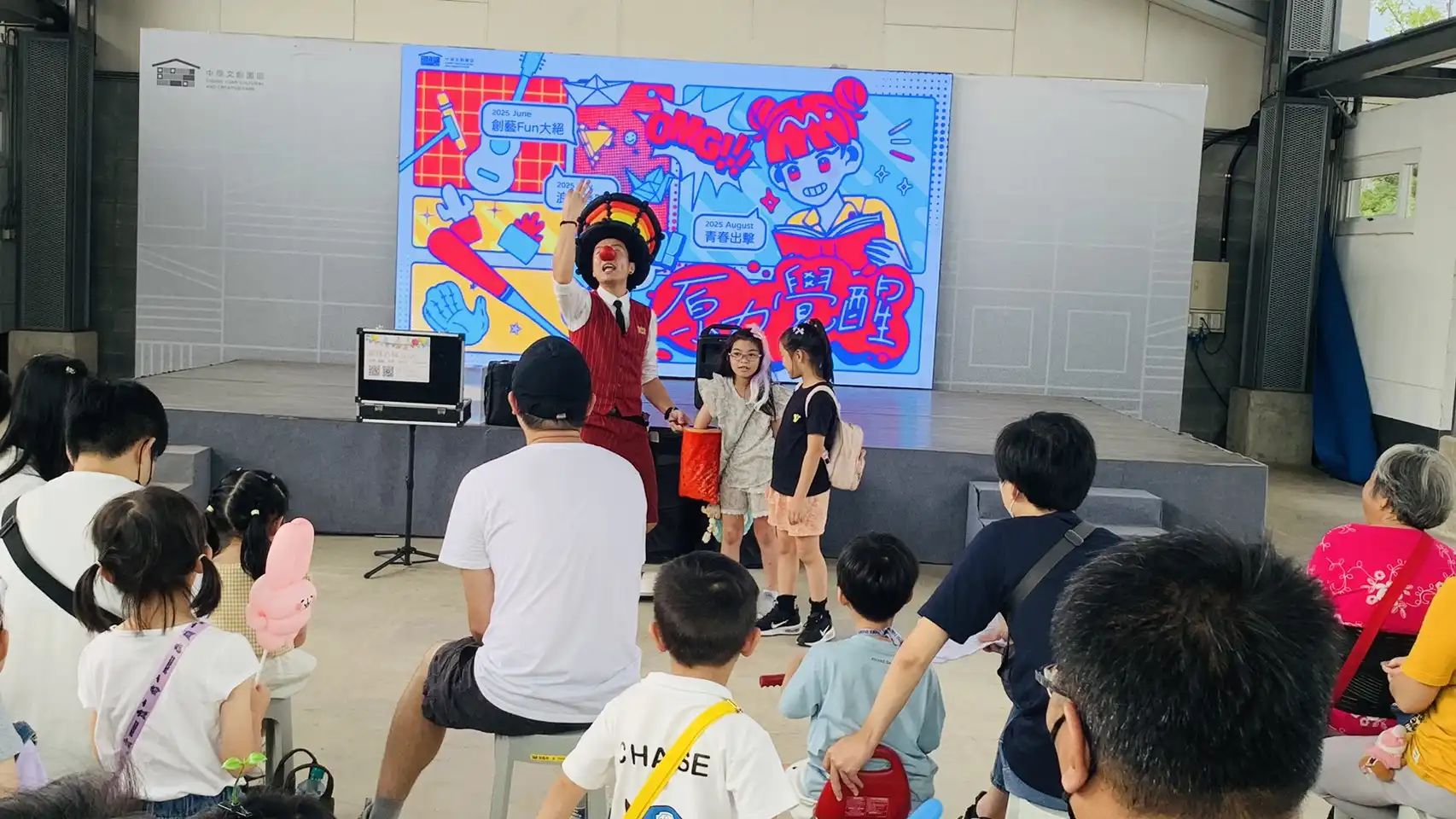 氣球大叔於桃園中原文創園區舞台上與台下觀眾互動，戴著小丑紅鼻子，表演生動有趣